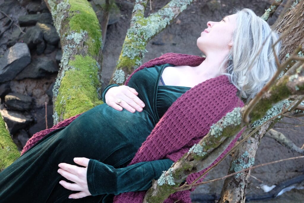 Photo de Johanna Sandretto enceinte en extérieur. Se reposant contre un arbre en pleine nature.